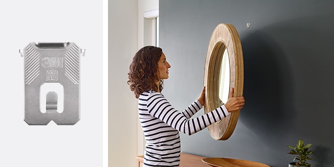 Kvinne som henger et rundt trespeil på en mørk vegg og bruker 3M CLAW™ bildeopphenger for gipsplater
