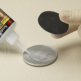 Lær om trinn 2, velge substrater og materialer, i 3M ASPEC-metoden. Bilde av lynlim som påføres mellom runde metall- og skumplater.