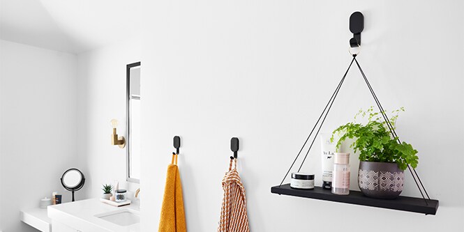 En vegg på et bad med 3M CLAW™ gipskroker der det henger en plante og håndklær på veggen.
