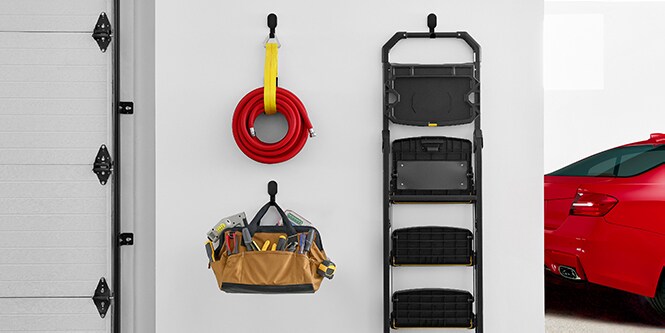 En vegg i en garasje med 3M CLAW™ gipskroker der det henger en slange, en stige og en campingstol.
